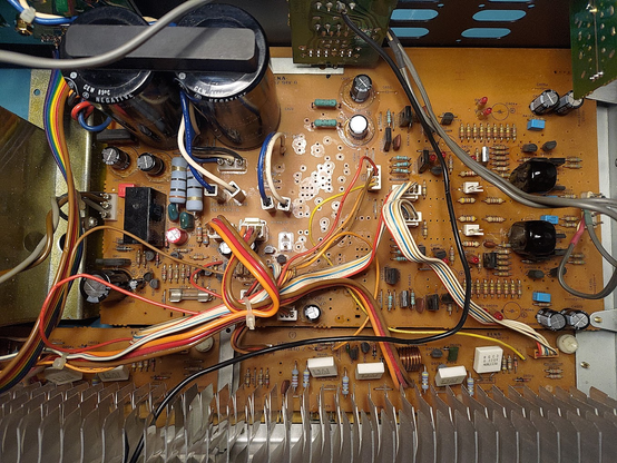 The main PCB of a Luxman L-525 amplifier. There are a lot of electronic components, all THT (no surface-mount devices). Most of the replaced electrolytic caps are smaller than their predecessors were, which is visible due to the silk screen markings for the original components. At the right edge there are four small blue rectangles, which are polypropylene foil capacitors, that have replaced big chunky (and sensitive) polystyrol capacitors.
