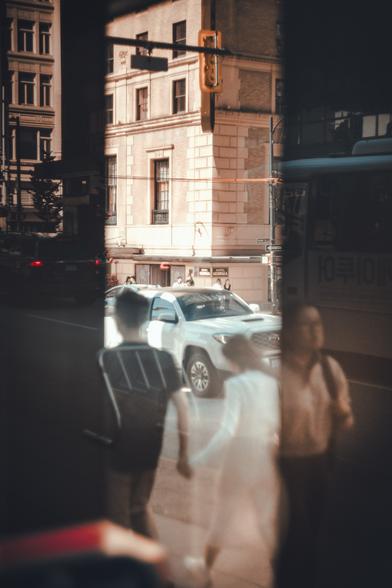 A couple pass through a glass archway along Georgia Street with buildings illuminated behind.