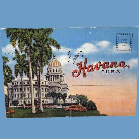 A colorful postcard labeled “Souvenir of Havana, Cuba” with a rectangle in upper right that says “PLACE STAMP HERE” and a few lines to write an address. A photo of the National Capitol Building in Havana colorized to highlight flowers, palm trees and a cloudy blue sky in the background.