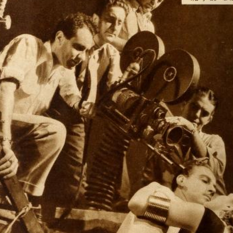 Un grupo de personas observando atentamente una antigua cámara de cine en un set de filmación.