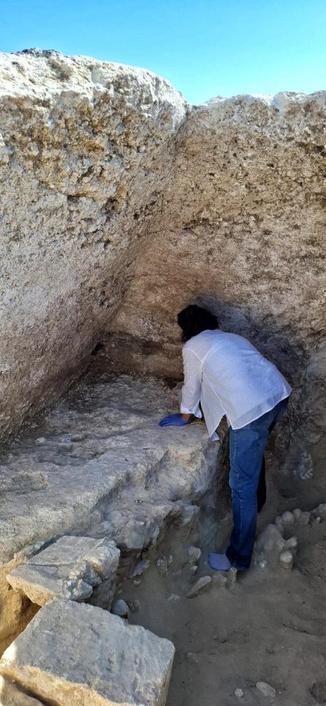 Un archeologo osserva e documenta all'interno di una tomba etrusca inviolata nella necropoli di Monterozzi, mostrando dettagli della banchina modanata e della struttura calcareo-fossile.