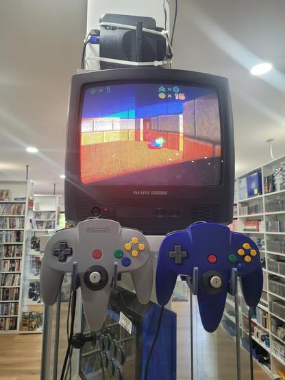 A CRT on a shelf with 2 N64 controllers mounted in front. The screen shows a Super Mario 64 beta mockup with Luigi sleeping on the floor. Above the screen is the N64 mounted sideways with an ED64 Plus flashcart.