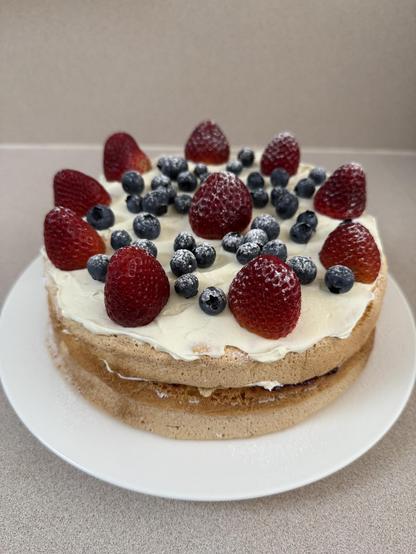 Sponge cake decorated with cream, strawberries, blueberries and dusted with icing sugar