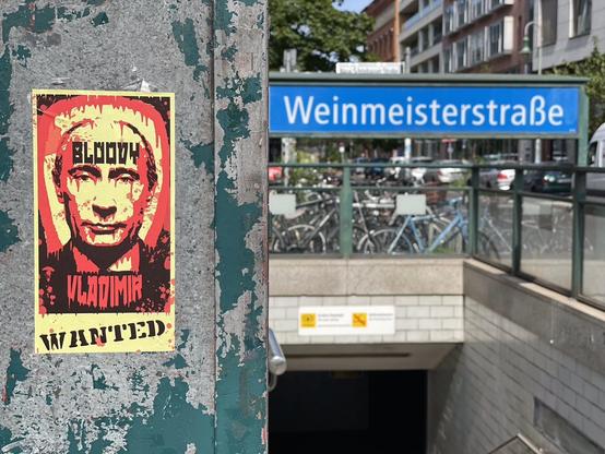 Metroeingang Weinmeisterstrasse. Daneben hängt einPlakat auf dem blutrot der Kopf von Putin abgebildet ist. Zusätzlich die Worte Bloody Vladimir wanted