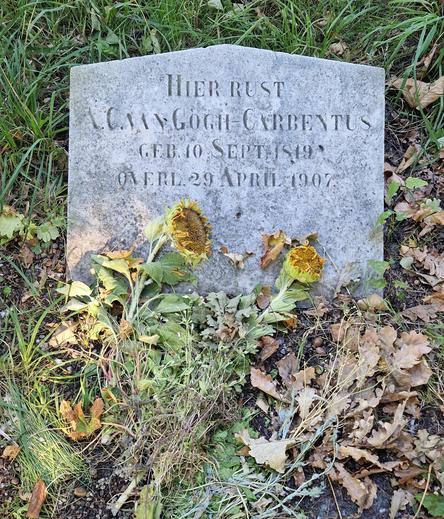 The grave of the mother of Vincent van Gogh, Anna van Gogh-Carbentus (1819-1907), at the Groenesteeg cemetery  in Leiden. A small simple headstone with her name and dates stands in rough grass. A couple of wilted sunflowers lie against the stone.