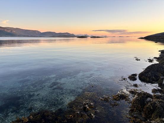 Sunset over a transparent sea water, with hills in the background.