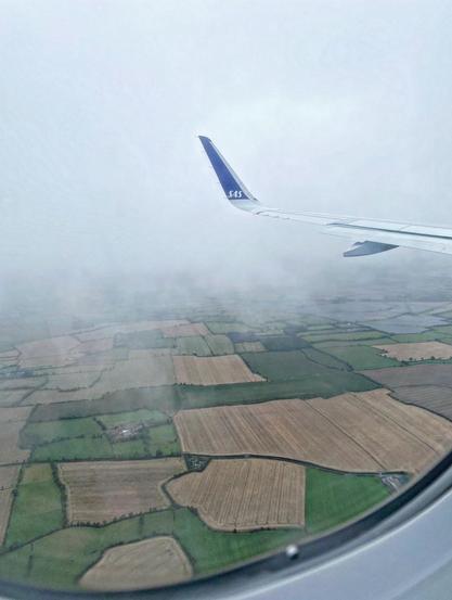 Vy från ett flyplansfönster där man ser en SAS-vinge och typiska irländska små åkrar i olika gröna och brunbeiga färger.