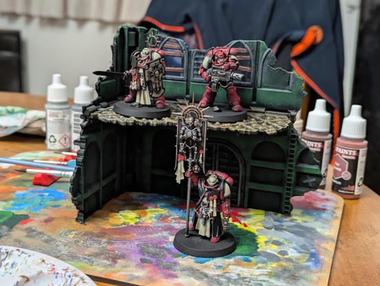 Painted Warhammer 40k minis on a piece of scenery. Three Space Marines painted as Blood Ravens in front of a green ruin.