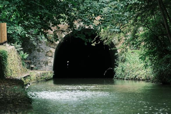 Entrance to tunnel on a canal, only space for boats, old brickwork all around and overgrown.