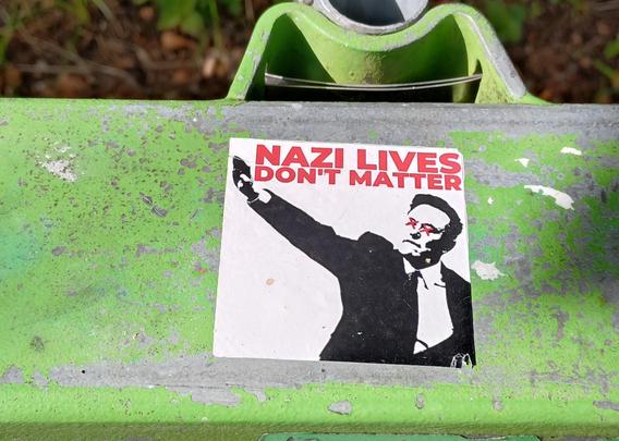 Foto, Sticker: Monochrome Abbildung von Elmo Musk bei der Antrittsfeier seines Bros Donald, bei welchem er den Hitlergruss macht. In rot darüber:
«NAZI LIVES DON'T MATTER»