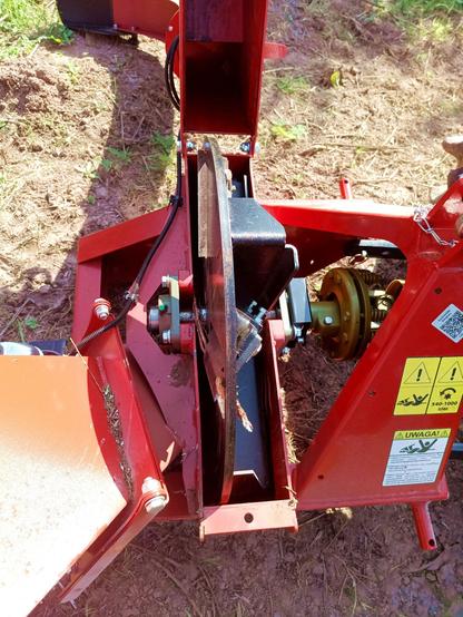 A tractor attached, PTO driven woodchipper in red. The cutting wheel housing is flipped open for maintenance. Inside a shaft riding on two bearings with a 40kg flywheel on which four adjustable blades are mounted and on the other side heavy steel fan/sweep blades that produce enough draft to blow/push the woodchips out without clogging.