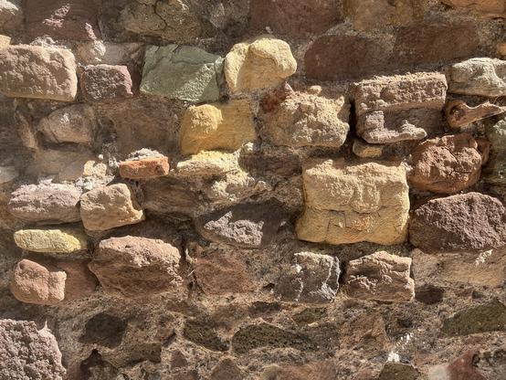 Ansicht einer alten Mauer, etwas ausgewaschen, mit rechteckigen Steinen, unterschiedlich groß , in verschiedenen Farbschattierungen.
