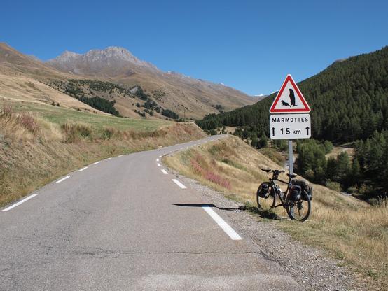A touring bike leaning against a sign that says "attention, marmots for the next 15km".