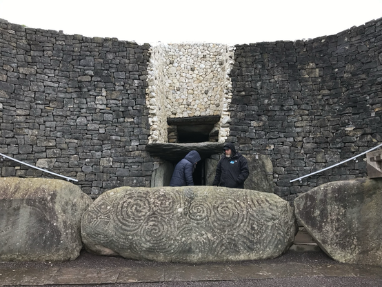 The entrance at Newgrange.  Stones with spiral artwork laying down in front of the entrance.