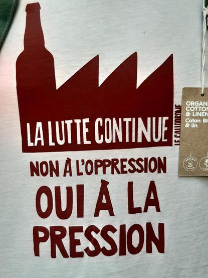 Tee shirt avec un dessin d'usine dont la cheminée est une bouteille de bière avec inscription : la lutte continue, non à l'oppression, oui à la pression.