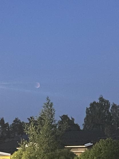 pimenevä kuun sirppi vielä valoisalla iltataivaalla.