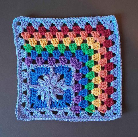 A colorful granny square. 
A star design in the lower left corner in blue and pastel purple
A granny stitch rainbow on two sides and framed with the pastel purple as granny stitch around everything