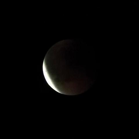 Mustalla taivaalla pimentynyt, punertava kuu jonka laita alavasemmalla alkaa kirkastua.