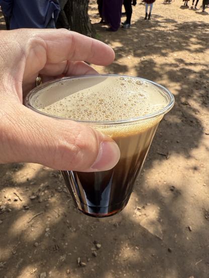 A plastic cup of dark beer with a thick foamy head