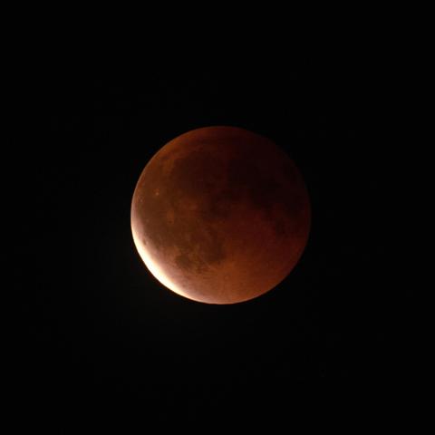 Eclipsed moon in the dark sky, at the bottom left the moon has already moved out of the umbra.