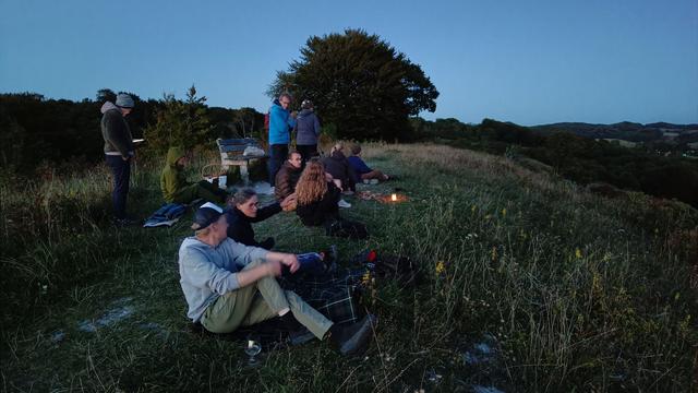 omkring 20 mennesker forsamlet på en bakketop i den sidste aftensol.