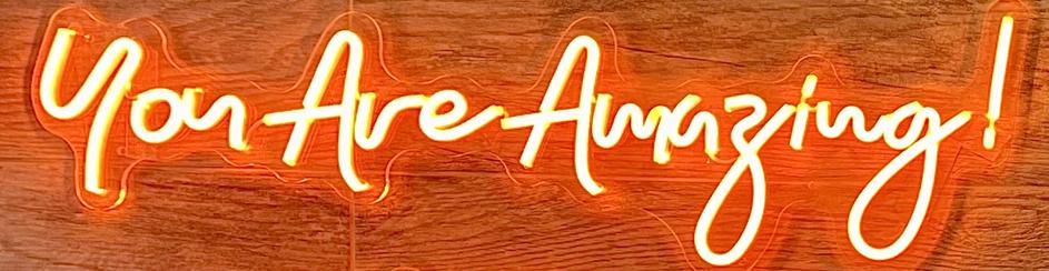 You Are Amazing! Red neon sign in cursive on wood wall.