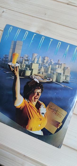 Pochette de l'album vinyle Breakfast In America de Supertramp sorti en 1979 montrant une serveuse hilare tenant à bout de bras un verre de jus d'orange, un menu breakfast in America dans l'autre main, dans une pose rappelant la statue de la liberté.  À l'arrière, tout un bric-à-brac de vaisselle disposés en forme de New-York stylisée. 
[EN] The cover of Supertramp's 1979 vinyl album Breakfast In America shows a hilarious waitress holding a glass of orange juice at arm's length, a breakfast in America menu in the other hand, in a pose reminiscent of the Statue of Liberty.  At the back, a jumble of crockery in the shape of a stylised New York.