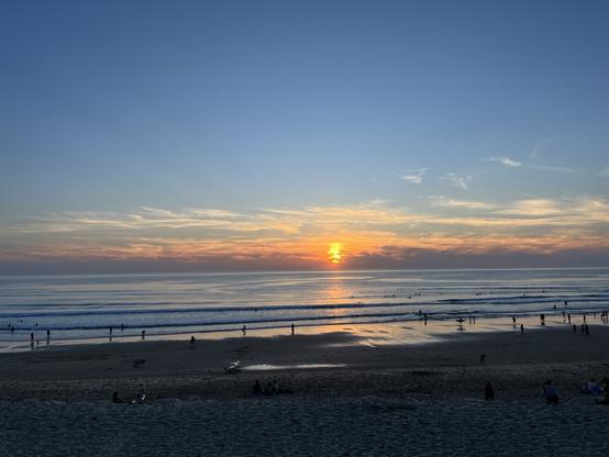 Breiter Sandstrand mit Blick auf den Atlantik, eine regelmäßige Brandung, am Horizont versinkt die Sonne im Meer.