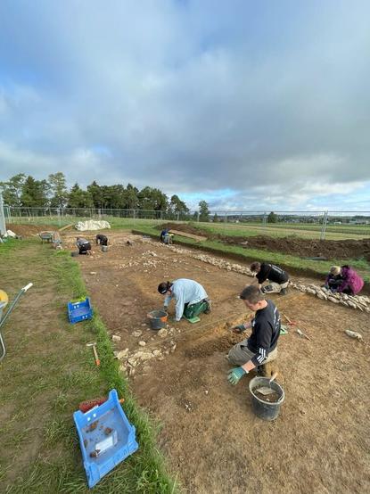 Un gruppo di archeologi impegnato negli scavi in un sito archeologico, con attrezzature e materiali disposti ordinatamente nel terreno.