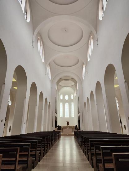 View down the nave. The church is austere and minimalist with blank, completely white walls and simple circles and ovals for windows and arches. Otherwise it has the expected architectural elements of a cathedral.