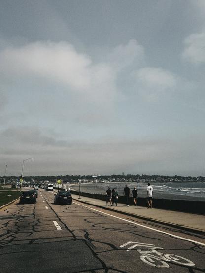 A scenic highway road by the ocean with a bike lane and a group of walkers walking by the ocean