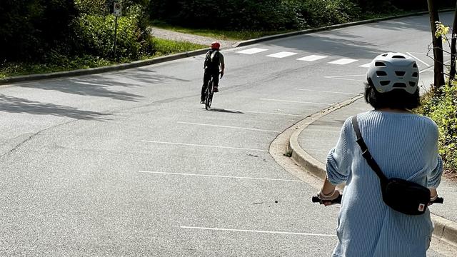 Two cyclists on a two-lane paved road descend and turn right on a hill.