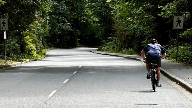 Single cyclist on a two-lane paved road heads down a hill.