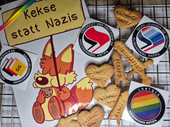 Der gezeichnete Fuchs von Fuchskind hält ein Demoschild mit der Aufschrift "Kekse statt Nazis" in die Luft. Das Bild wird umrahmt mit Keksen in verschiedenen Formen. Darauf gestempelt finden sich die Schriftzüge Demokratie, Klimaschutz und FCKAFD. Verschiedene AntiFa-Aufkleber von Radotto ergänzen das Bild. U.a. "Überreizt und trotzdem da - hochsensible AntiFa", "Nazis leugnen die Gefahr - Klimschutz ist AntiFa", "Artikel 1 und deshalb da - Menschenrecht ist AntiFa", "LGBTQIA - Regenbogen AntiFa"