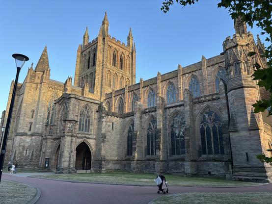 View of the outside of Hereford Cathedral. The stumped bell tower is to the left of the picture with the nave to the right. The sly above is blue.