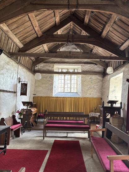 Inside Craswall church which is more a chapel than a church. The roof is wood with wooden beams and there are wooden benches with red cushions in the church.