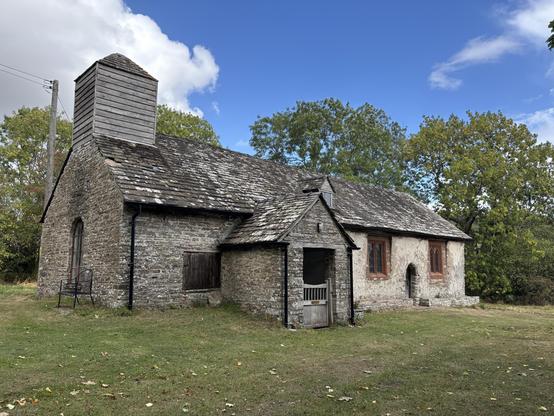 Outside view of the church in Craswall. The church looks ancient with dark grey stone and the bell tower is made of grey wood.
