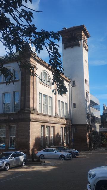 Tall, white Italian style tower on the side of a former school building, against a blue sky
