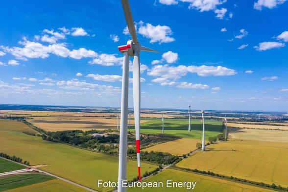 Windkraftanlagen stehen in der Landschaft vor blauem Himmel mit weißen Wölkchen.
