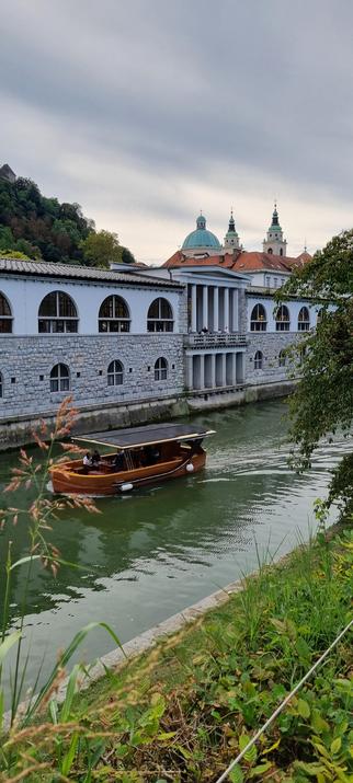 Foto zeigt ein Boot auf der Ljubljanica und die Plečnikove arkade im Hintergrund am Ufer