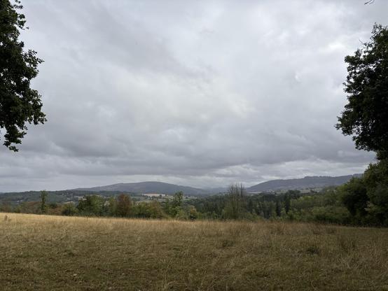 View over hills far in the distance. In the foreground is a brownish field. The sky is low and grey.