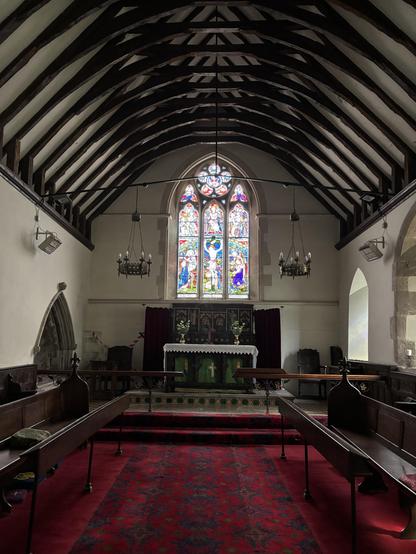 The inside of the church in Ewyas Harold with a high wooden roof and a beautiful stain glass window behind the altar.
