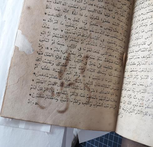 Page d'un livre ancien en caractères arabes sur laquelle se sont imprimées deux traces brunes laissées par une paire de ciseaux ou des bésicles avec un manche ?