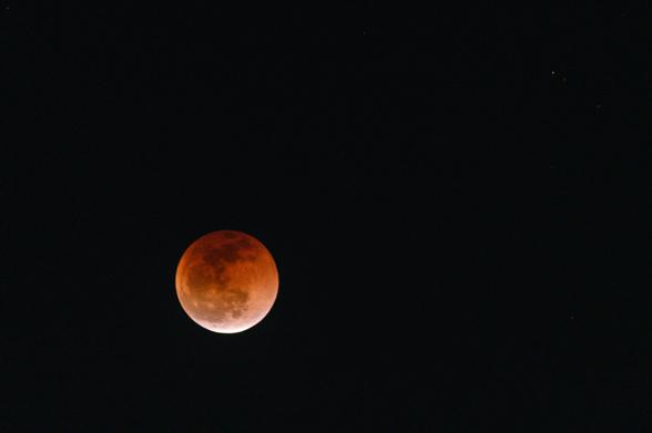 A partial lunar eclipse is depicted, showing a reddish moon against a dark sky, with a few distant stars visible.