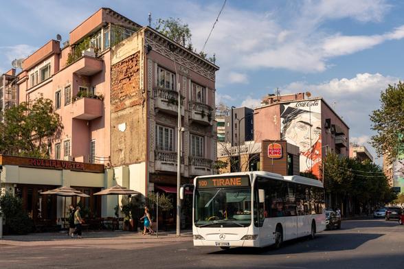 Bus to Tirana in front of buildings with murals.