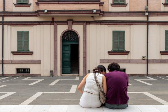 Couple sitting with their backs to the camera in front of a building with green doors and windows.