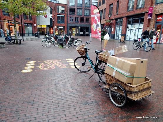 Dutch bicycle parked in a Dutch city centre location. It's pulling a trailer stacked up with cardboard boxes which contain bicycle parts. This is how we send all our parcels. We don't have any motorised vehicles.