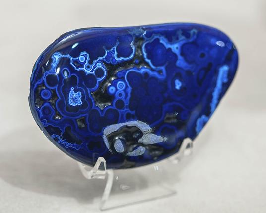 Polished chunk of azurite on matrix. Specimen is about 4” long, seen through the glass display case at a Tucson Gem and Mineral Show. It’s deep blue and shaped like a fat bean. Likely the blue azurite formed over botroyidal rounded lumps of malachite. This piece is heavily polished to show rounded curves and  concentric circles of azurite layers built up on the malachite.