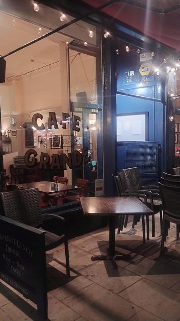 Looking through the window of Café Grande, their logo painted on the glass, late night, almost empty save a couple of late diners, chairs starting to be stacked on tables for the night