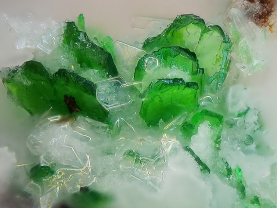 Photograph of tabular, bright green cystals of kosmochlor with white crystals found in a vug. Location: Feuerberg, Vulkaneifel, Germany. Image credit: Volker Betz